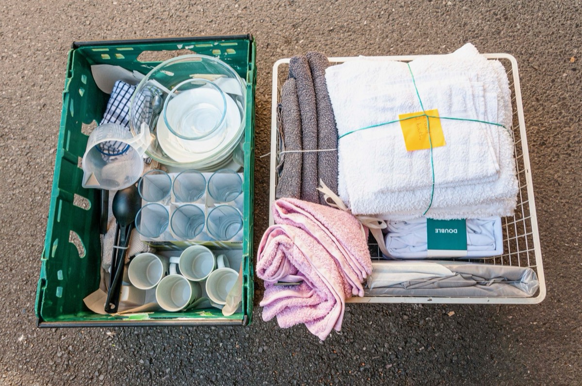 A starter pack of crockery, glasses and utensils beside a basket of towels and bedding